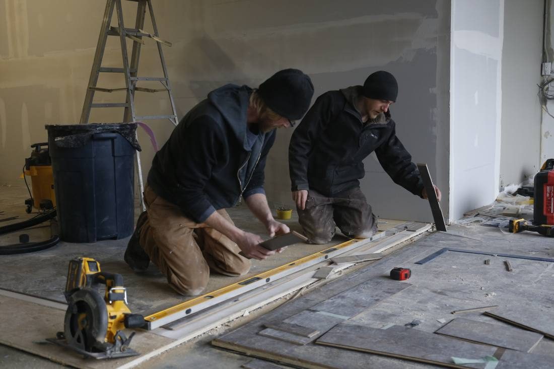 Two people kneeling on the floor cutting flooring to size